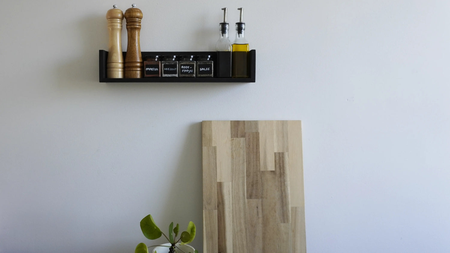 Sfeerbeeld van een zwevende wandplank met opstaande randen aan de zijkant in een zwarte kleur. Op de plank staan diverse kruidenpotjes, olieflesjes en een peper- en zoutmolen.