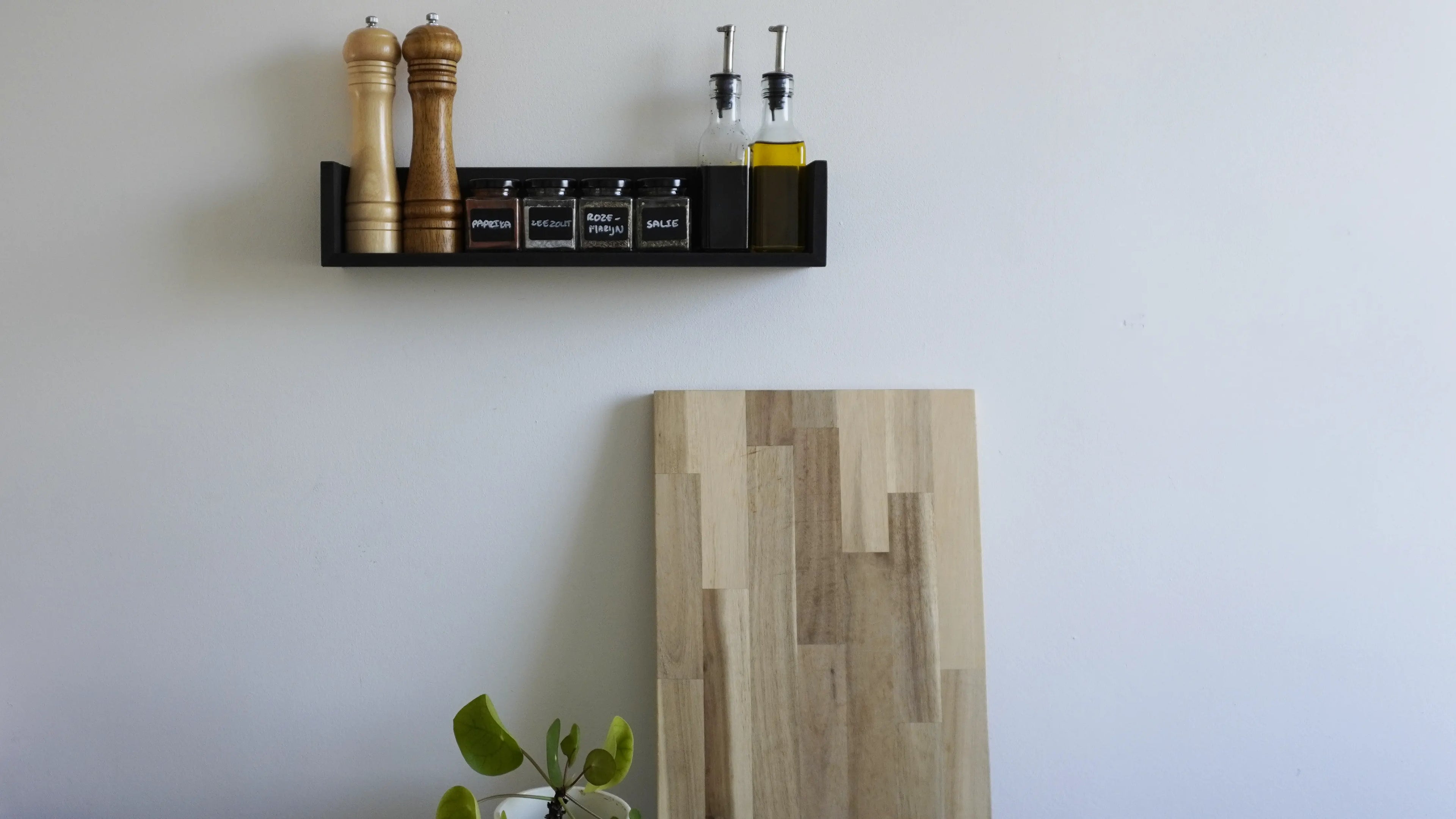 Sfeerbeeld van een zwevende wandplank met opstaande randen aan de zijkant in een zwarte kleur. Op de plank staan diverse kruidenpotjes, olieflesjes en een peper- en zoutmolen.
